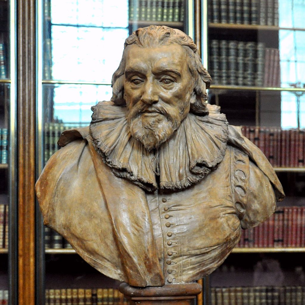 Photograph of a bust of Robert Cotton sitting in front of a glass-front bookcase.